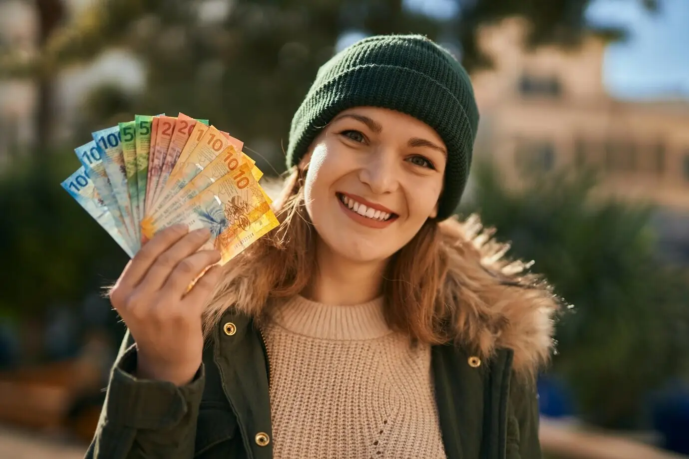 Junges kaukasisches Mädchen lächelt glücklich und hält Schweizer-Franken-Banknoten in der Stadt.